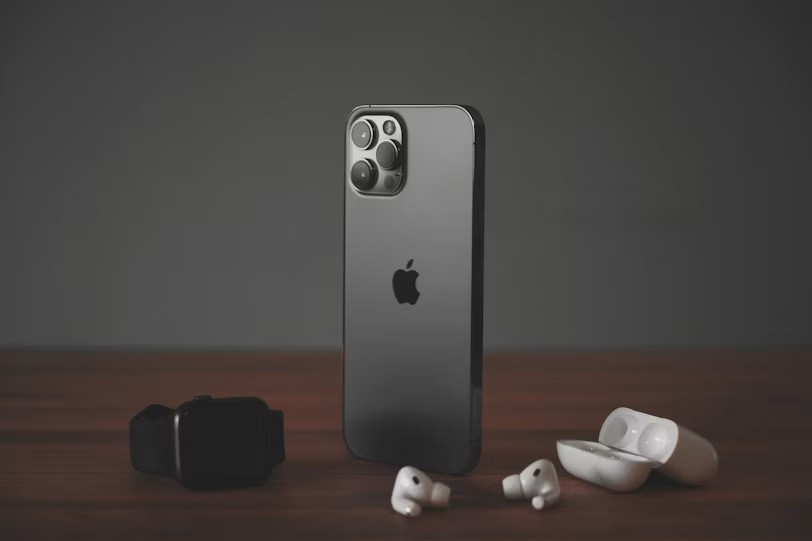 A smartphone, a smartwatch, and wireless earbuds on a wooden surface